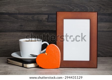 blank frame poster on the wooden table with cup of coffee, book and heart