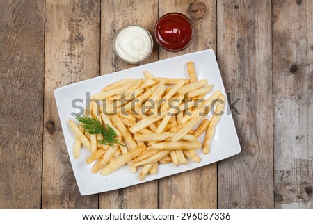 French fries on white dish on wooden background.