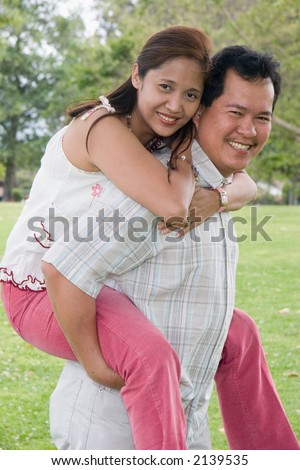 man giving his girlfriend a piggy-back ride on his back in a park