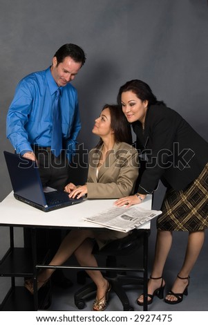 Three office workers, one man and two women standing around a desk in front of a computer having a discussion