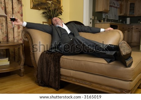 Man in a business suit sleeping on the sofa with a glass of red wine still in his hand