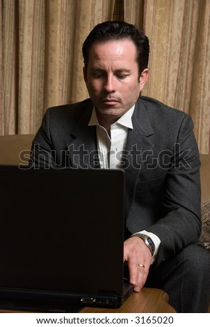 Man in business suit sitting on beige leather sofa looking at a laptop computer