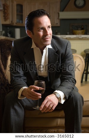 Man in a business suit sitting on the sofa drinking a glass of red wine