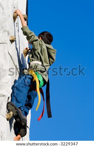 Young asian boy outside climbing on a rock climbing wall with clear blue sky in background