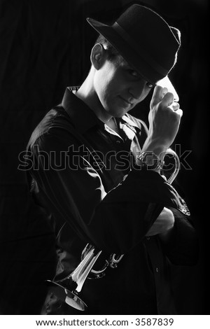 Handsome young man holding a trumpet wearing a black hat on black in black and white