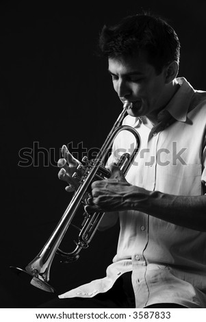 Handsome young man playing a trumpet on black background in black and white