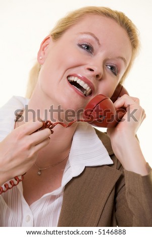 Close up of beautiful blond haired woman in business suit talking on an old style red phone with a laughing facial expression