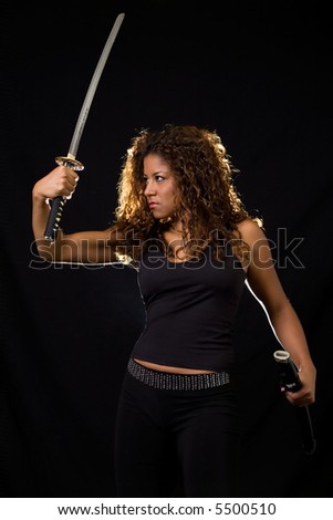 Attractive Hispanic woman wearing all black holding a samurai sword standing on black
