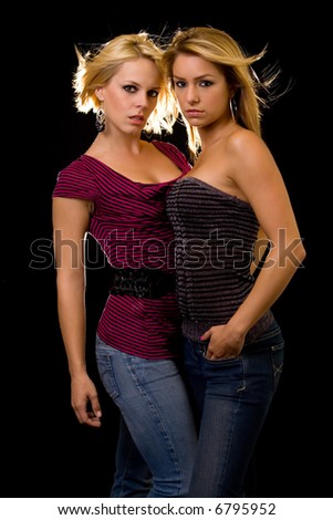 Portrait of a two young attractive women in casual attire with hair blowing standing close together on black