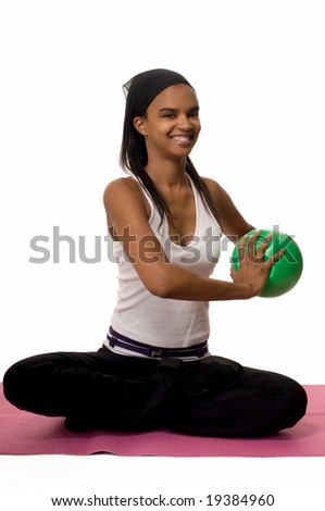 Attractive African American woman wearing head band and workout attire sitting cross legged on the floor holding a small green exercise ball