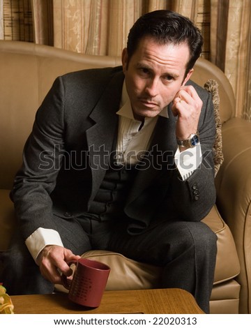 Man in a business suit sitting on the sofa holding a coffee cup thinking