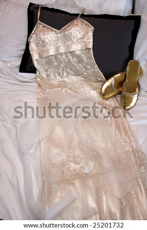 Woman\'s white wedding dress laid out beside gold shoes on bed
