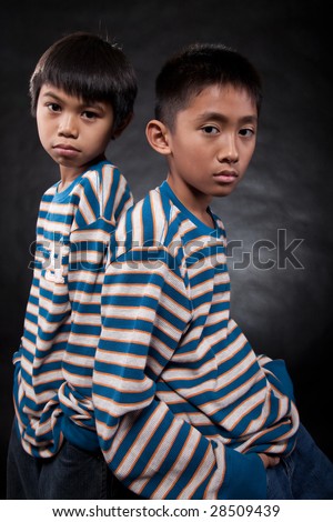 Two young eleven year old asian boys standing with backs together wearing matching shirts