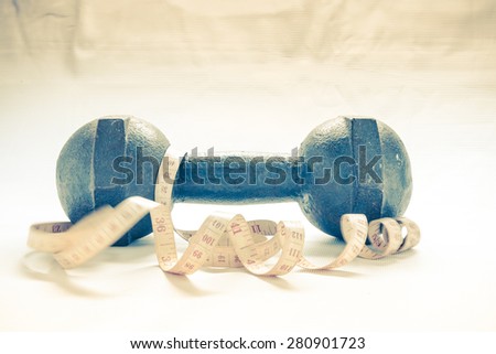Fitness concept - dumbbell with measuring tape with vintage retro picture style