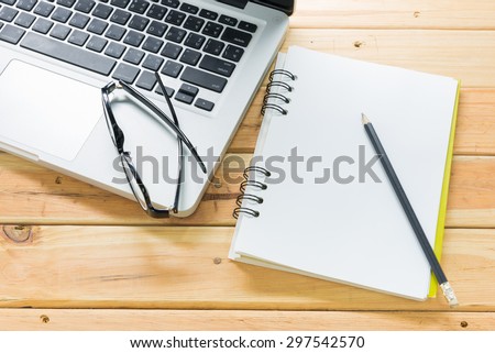 Overhead of open notebook with pen and glasses on a wooden desk