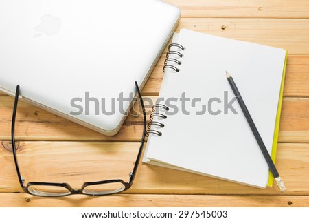 Overhead of open notebook with pen and glasses on a wooden desk
