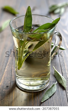 Glass of herbal sage tea made from freshly picked green sage leaves standing on a wooden surface