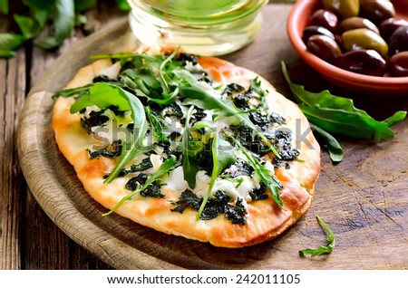 Homemade goat cheese and mozzarella pizza seasoned with basil puree and freshly picked arugula leaves. Fresh spring recipe.