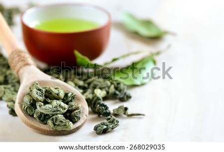 Wooden spoon with dried green tea leaves in it and a cup of green tea on a backstage