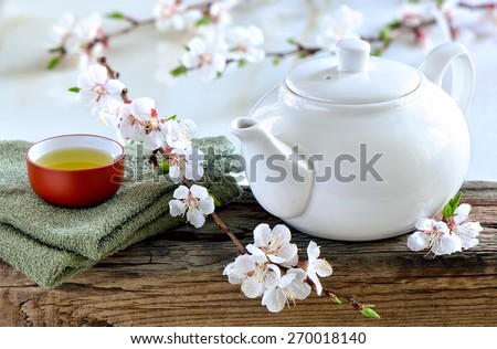 White teapot with freshly brewed green spa tea on wooden surface with a cup of healthy calming and detox tea decorated with spring blooming branches