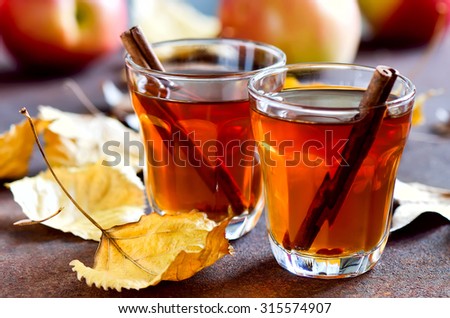 Apple cider with cinnamon sticks in glasses decorated with autumn yellow leaves
