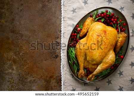 Festive traditional food, roasted chicken in an oval dish, decorated with rosemary and cranberries, there is a space for greeting or inviting text, view from above