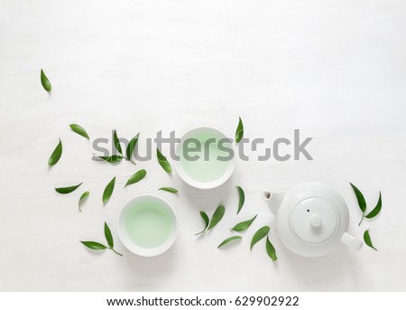 Tea freshly brewed in a teapot and two cups, surrounded with fresh tea leaves, top view composition, space for a text