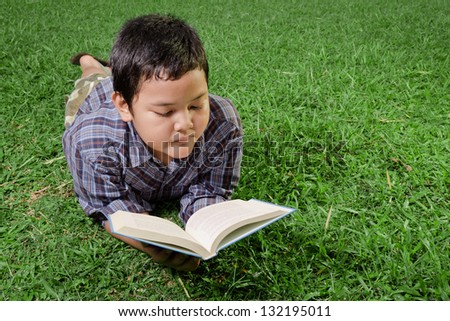 young asian boy reading a book in the park