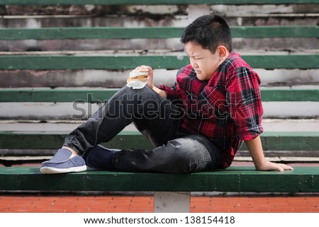 asian boy hold a muffin sandwich on a green concrete bench