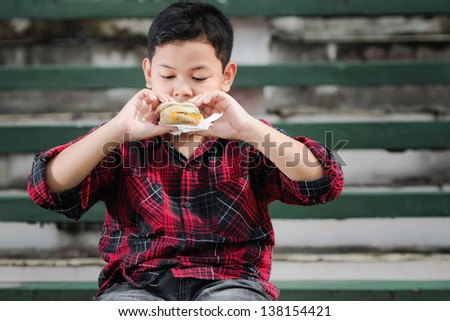asian boy eating muffin sandwich on a green concrete bench