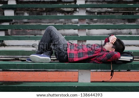 an asian boy sleeping on a concrete bench with hand over his forehead