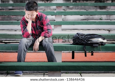 asian boy sitting on a concrete bench shows unhappy expression