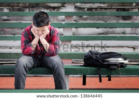 asian boy sitting on a concrete bench shows unhappy expression