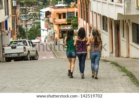 Three young Hispanic ladies sight seeing walking in the street, building in distance
