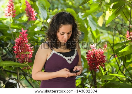 Young attractive Hispanic woman portrait outside green behind texting on a smart phone