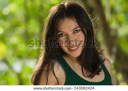 Young attractive Hispanic woman portrait outside green behind.
