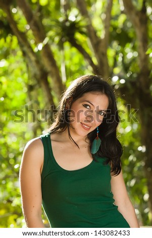 Young attractive Hispanic woman portrait outside green behind.