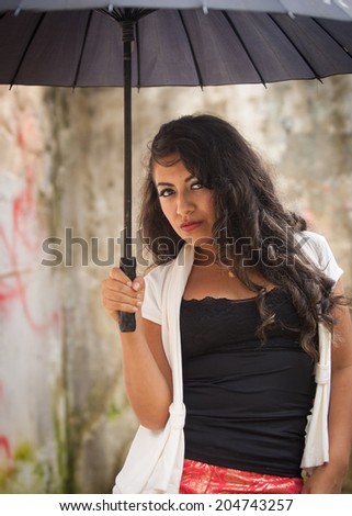 Young attractive Ecuadorian lady walking with black umbrella in the rain