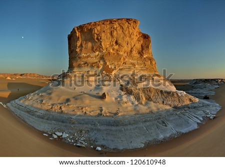 Towering limestone rock in the White Desert of Egypt. This white rock is circled by a sand dune. The photograph was taken at sunset in the Sahara desert