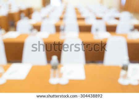 blurred image of many row of chairs set for conference, dinner or meeting event with large hall with people.