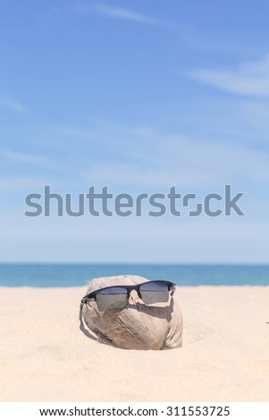 Sunglasses over coconut fruit on sandy beach under hot shiny sun light looked like a happy (tourist) man lying on the beach during holiday summer vacation on wonderful trip under bright blue sky.