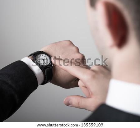 Man\'s hand in the suit pointing on his watch on a gray background