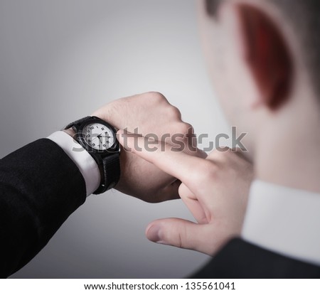 Man\'s hand in the suit pointing on his watch on a gray background
