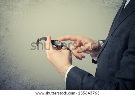 Man's hand in the suit pointing on his watch on a gray background