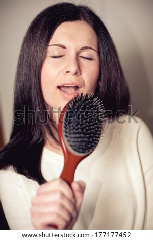 Young tousle-headed brunette pretending to sing with her hair brush as a microphone
