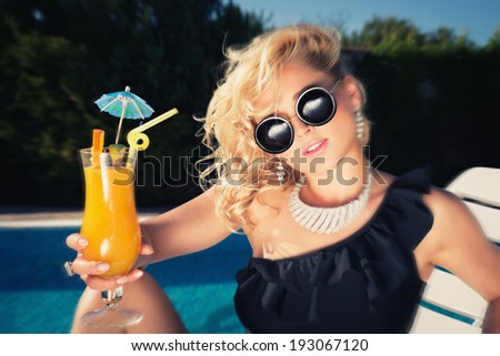 beautiful, suntanned, young woman drinking cocktail, and enjoys in the summer afternoon near the pool