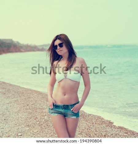 Outdoor fashion warm colors portrait of young sensual happy woman in jeans shorts, bikini and sunglasses. model posing. Photo toned style instagram filters