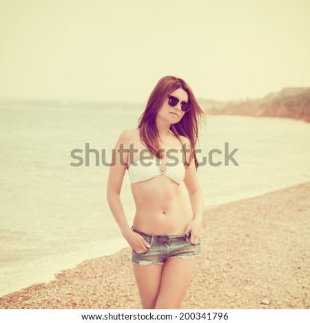 Outdoor fashion warm colors portrait of young sensual happy woman in jeans shorts, bikini and sunglasses. model posing. Photo with instagram style filters