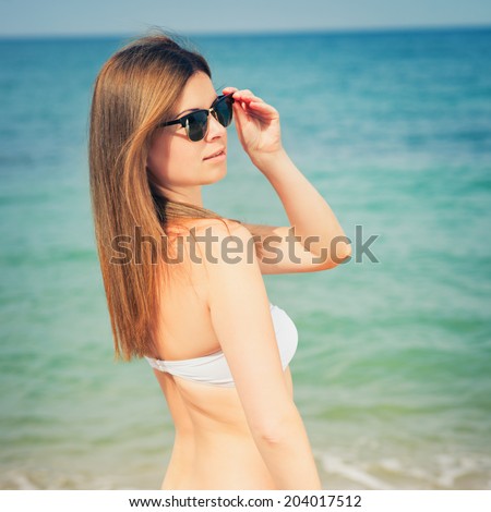 Outdoor fashion warm colors portrait of young sensual happy woman in jeans shorts, bikini and sunglasses. model posing. Photo with instagram style filters