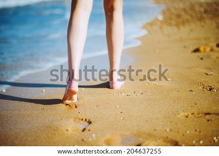 Woman walking barefoot on sunny beach in summer day